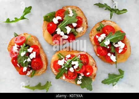 Crostini appetizers with cherry tomatoes, arugula, and cheese, above view on white marble Stock Photo