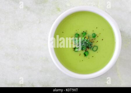 Creamy broccoli soup in a white bowl, overhead view on white granite background Stock Photo