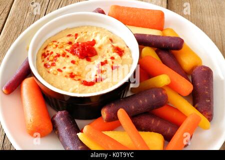 Plate of baby rainbow carrots with hummus dip, close up on a rustic wooden background Stock Photo