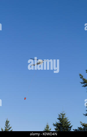 Helicopter against blue sky, flying with empty bucket after dropping water on forest fire. Stock Photo