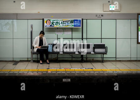Woman in Tokyo sitting on subway train platform using laptop Stock Photo