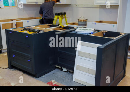 Repair man In Overalls Repairing Cabinet Hinge In Kitchen Stock Photo