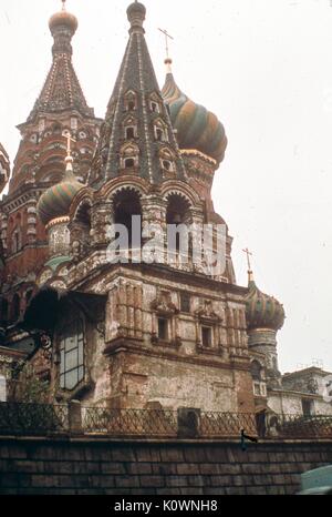 Detail view facing north of several of the intricate domes and towers of Saint Basil's Cathedral, in Red Square, Moscow, Soviet Russia (USSR), November, 1973. In the background from left is the Central Chapel tower, with the Chapel of the Trinity onion dome to the right. In the foreground is the masonry of the Bell Tower and lower exterior wall. Stock Photo