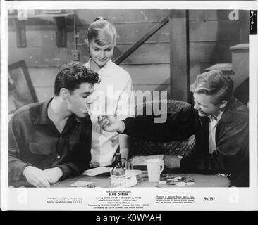 A movie still scene from 'Blue Denim' (1959 20th Century Fox film), showing three teenagers, two boys seated with one lighting up the cigarette of the other while the young blonde girl looks on with a smile, 1959. Stock Photo