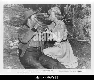 A movie still scene from 'The Tougher They Come' (1950 Columbia Pictures film), showing a worn-out man down on the ground in a sitting position while a woman with smudges on her face and dress holds up a flask of water for him to drink, 1950. Stock Photo