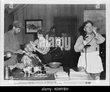 A movie still scene from 'The Tougher They Come' (1950 Columbia Pictures film), showing seven adults, two injured men seated on a chair with two people attending to each, while another is on the phone requesting for more assistance, 1950. Stock Photo