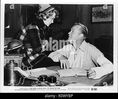 A movie still scene from 'The Tougher They Come' (1950 Columbia Pictures film), showing a man sitting who was reading a book conversing with a woman standing in front of him, 1950. Stock Photo