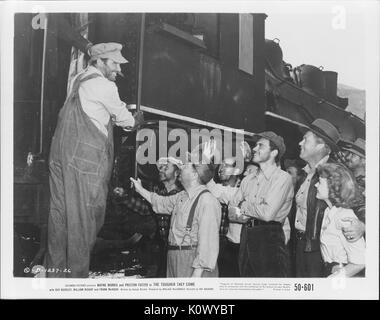 A movie still scene from 'The Tougher They Come' (1950 Columbia Pictures film), showing several people standing beside a train, some waving good-bye to a man standing on an entrance step of the train, 1950. Stock Photo