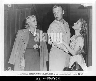 A movie still scene from 'The Tougher They Come' (1950 Columbia Pictures film), showing a young couple holding each other being interrupted by a young blonde woman in a long coat hang over her dress, 1950. Stock Photo