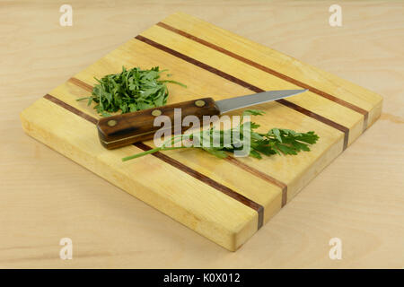 Chopping fresh parsley with kitchen knife on wooden cutting board Stock Photo