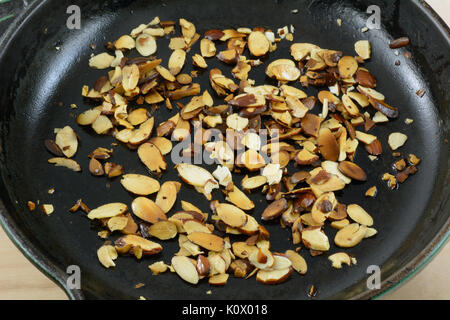 Roasting sliced almonds in olive oil in cast iron frying pan skillet Stock Photo