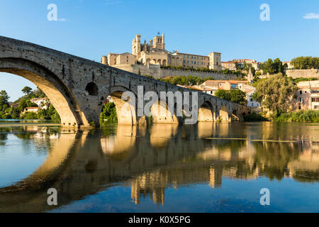 Views at sunset of the French city of Beziers, with trees and the old bridge reflected over the river Orb, and the 13th-century Cathedral of Saint Naz Stock Photo