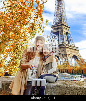 Autumn getaways in Paris with family. smiling mother and child travellers on embankment in Paris, France taking selfie using selfie stick Stock Photo