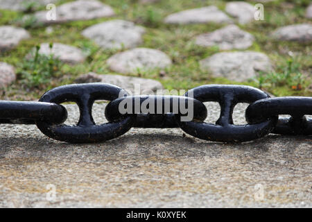 A black metal chain with large links lies on concrete slabs on the ground. Stock Photo