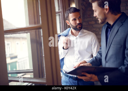 Two young businessmen in office standing near window and talking Stock Photo