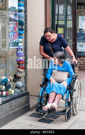 An elderly 97 year old woman in a wheelchair with her carer or assistant shopping for wool in Birchington, Thanet, Kent. Stock Photo