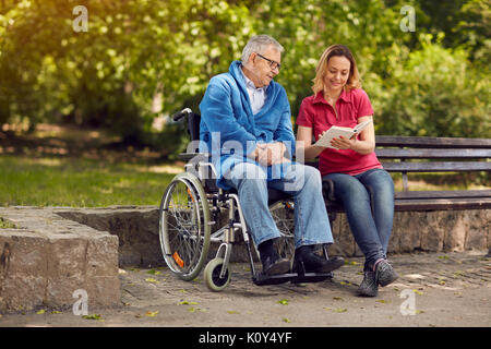 Spending time together reading book outdoor cheerful daughter and disabled father in wheelchair Stock Photo