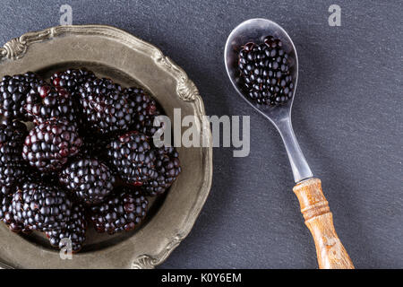 healthy blackberries in plate and spoon on dark table background Stock Photo