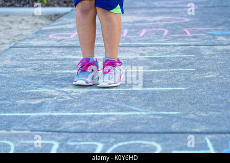 Children playing in the park with hopscotch and following chalk drawings on the pavement Stock Photo