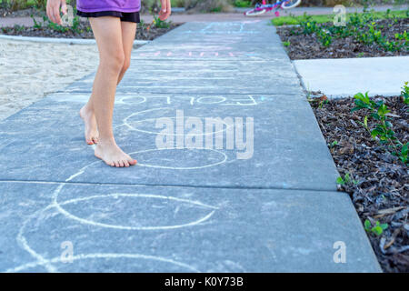 Children playing in the park with hopscotch and following chalk drawings on the pavement Stock Photo