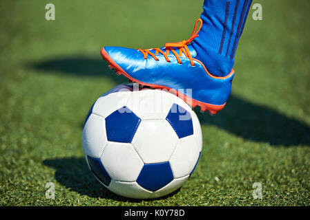 Foot of a soccer player in a football boot on a ball on an artificial green lawn of the stadium Stock Photo