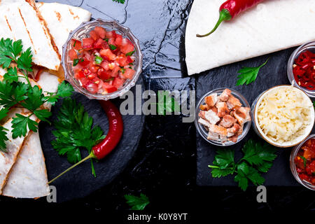 Mexican quesadilla and ingredients with salsa on black slate stone plate. Stock Photo