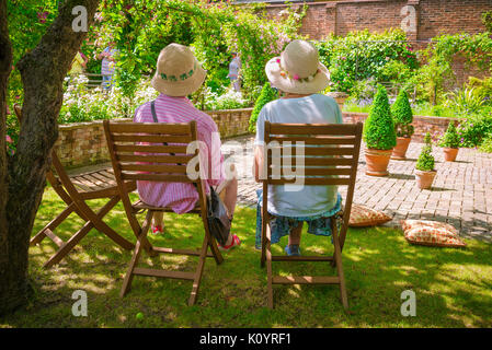 Senior women friends, rear view in summer of two women sitting together under shade in an English garden, Suffolk, UK. Stock Photo