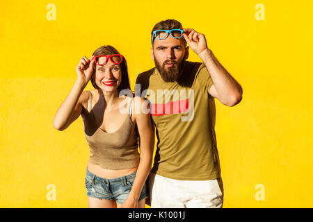 Funny couple in casual style clothes and color glasses looking at camera. Isolated on yellow background , indoor studio shot Stock Photo