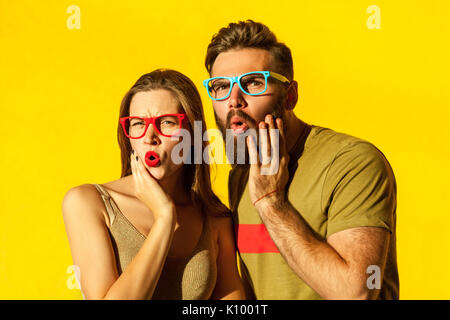 Bearded young adult man and beautiful freckled girl, touching hes chin, have surprised faces and looking at camera. Yellow background. Studio shot Stock Photo