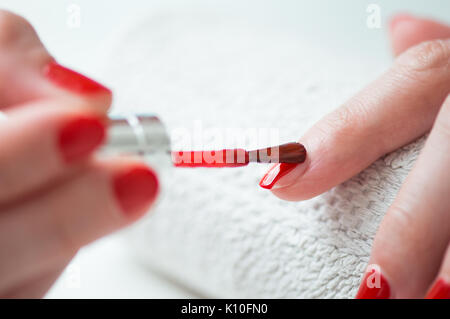 Closeup of a woman painting her nails with red nail polish Stock Photo