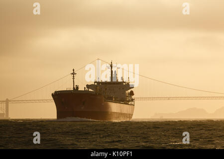 Giant oil tanker ship slips under golden gate bridge at sunset heading out to sea Stock Photo