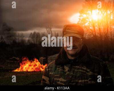 A man in uniform armed with a fire. Smile of the prankster. In the background, the building burns. Stock Photo