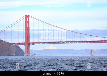 Golden Gate Bridge and sailboat with red sails in light fog