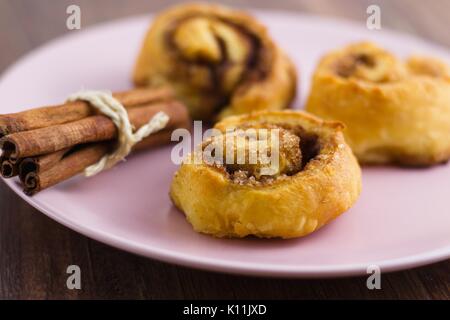 Cinnamon rolls and a pack of cinnamon sticks on pink plate ready to eat Stock Photo