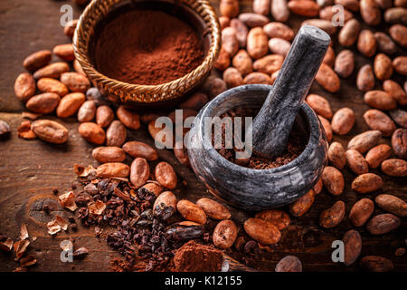 Cocoa concept with stone mortar and pestle with raw, peeled, and crushed Theobroma cacao cocoa beans Stock Photo