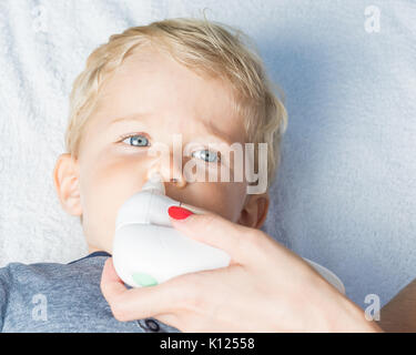 Mother using baby electric nasal aspirator. She is doing a mucus suction to twenty months baby boy. Stock Photo