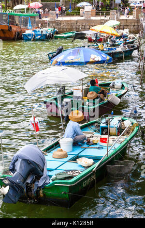 HONG KONG - JULY 13, 2017: Fishermen in boats alongside the Sai Kung harbor sell their live seafood catch to the public on the pier. Vertical orientat Stock Photo