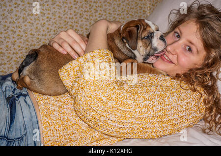 A pretty young woman lying down, holding a beautiful, nine weeks old, red British bulldog male puppy with a white face. Stock Photo