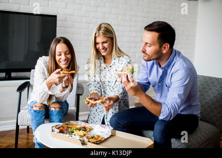 Small group of young friends eating pizza in the room Stock Photo