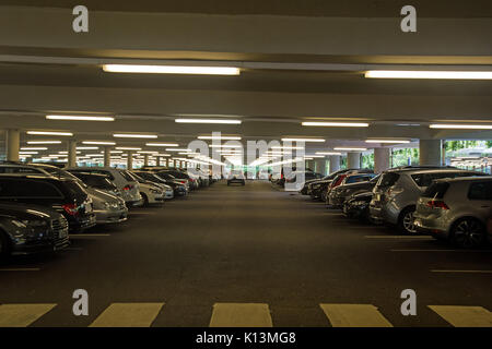 Well lit large underground car park with cars parked and a crossing for pedestrians. Stock Photo