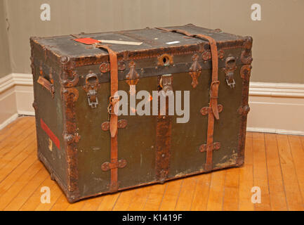 an old vintage dark green and brown travel chest or trunk with leather straps sits on a wood floor Stock Photo