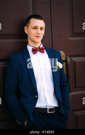 Groom wearing blue suit bowtie at the red door Stock Photo - Alamy