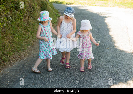 Three young French girls, sisters, walk hand-in-hand holding hands along a French country road in the summer. They are aged 3, 5 and 7 years old.(89) Stock Photo