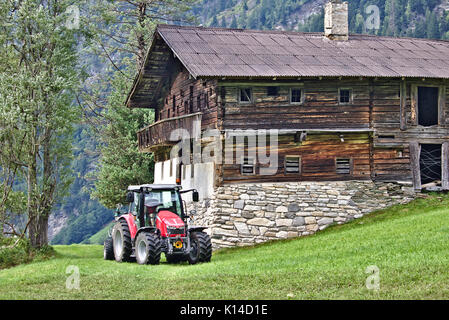 Derelict wooden farmhouse on a green grassy slope with red tractor Stock Photo