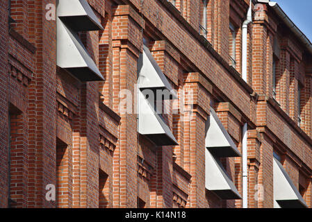 Sunlit red brick wall with narrow windows and metal air-conditioning wall vents Stock Photo