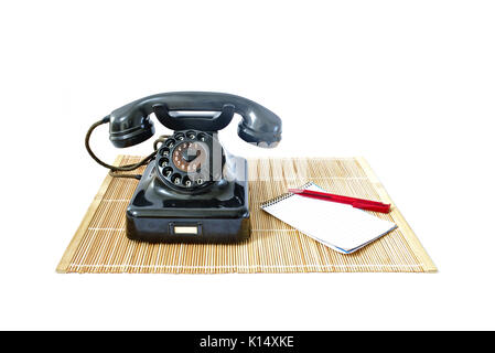 Vintage telephone on rattan mat with red pen and notepad with copyspace isolated on white background Stock Photo