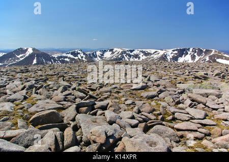 Boulders and rocks on the summit of Ben Macdui with snow-covered mountain ridge in the background Stock Photo