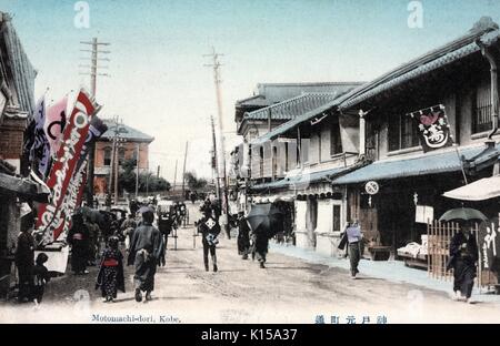 Hand colored post card of Motomachi-dori, showing people and carts on a road lined with stores, Kobe, Japan, 1912. From the New York Public Library. Stock Photo