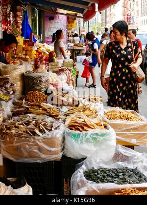 Pedestrian shoppers looking at items for sale in front of a Chinese food market shop, sidewalk in Chinatown, New York, NY, USA. Stock Photo