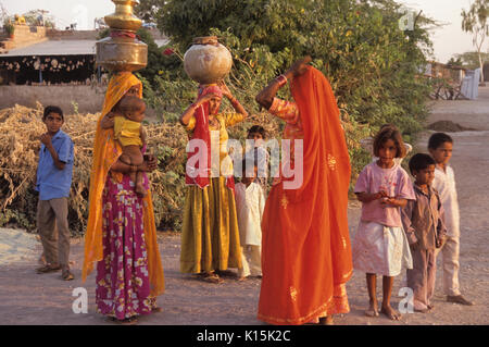 Bishnoi women (carrying pots of water on head) and children in village near Jodhpur, Rajasthan, India Stock Photo